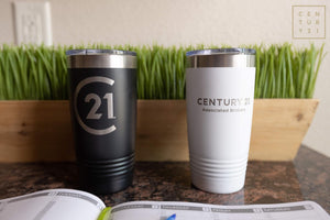 Two Kodiak Coolers Custom Tumblers 20 oz with your Logo or Design Engraved - Special Bulk Wholesale Pricing - Pack of 72 Pieces - 1 Color - $12.49 Each, one black and one white, placed on a counter next to a calendar and a planter with green grass.