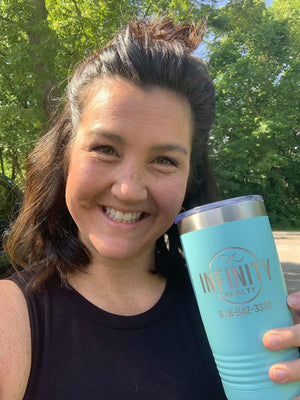 A woman with dark hair holds a turquoise tumbler with "Infinity Realty" and a phone number printed on it, smiling outdoors with trees in the background. The Custom Tumblers 20 oz with your Logo or Design Engraved - Special Bulk Wholesale Pricing - Pack of 96 Pieces - 1 Color - $12.49 Each by Kodiak Coolers showcases her brand effortlessly.