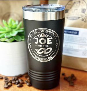 A black travel mug with the label "Joe on the Go Coffee Co." sits on a table next to a small green succulent and a few coffee beans. A brown paper coffee bag is partially visible in the background, making it an ideal option for corporate gifts or Custom Tumblers 20 oz with your Logo or Design Engraved - Special Bulk Wholesale Pricing - Pack of 24 Pieces - 1 Color - $16.63 Each by Kodiak Coolers.