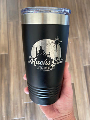 A hand holds a black insulated tumbler with a clear lid, featuring the logo and text, "Machs Gute Pub and Grille Bethlehem, PA." The background is a wooden floor. These Kodiak Coolers Custom Tumblers 20 oz with your Logo or Design Engraved - Special Bulk Wholesale Pricing - Pack of 72 Pieces - 1 Color - $13.87 Each are perfect for promoting your brand with low minimum orders.