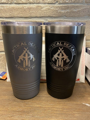Two Kodiak Coolers Custom Tumblers 20 oz with your Logo or Design Engraved - Special Bulk Wholesale Pricing - Pack of 24 Pieces - 1 Color - $16.63 Each with "Tactical Defense Armory Inc." logos displayed on a table against a brick wall background. One mug is gray, and the other is black. Perfect for corporate gifts or wholesale custom tumblers orders.