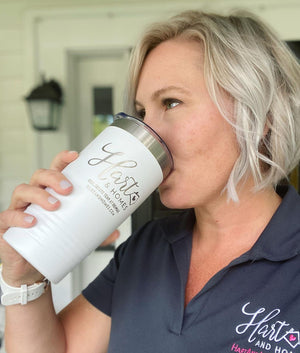 A person with short blonde hair drinks from a large white tumbler with the laser engraved logo "Hart & Home" while wearing a dark polo shirt. The tumbler is one of Kodiak Coolers' Custom Tumblers 20 oz with your Logo or Design Engraved - Special Bulk Wholesale Pricing - Pack of 48 Pieces - 1 Color - $14.56 Each.