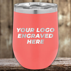 A coral-colored insulated tumbler by Kodiak Coolers sits on a wooden surface with "Your Logo Engraved Here" on the front. These stylish and functional engraved tumblers are perfect promotional gifts for any business, featuring laser-etched design and no setup fees. Limited time offer available!.