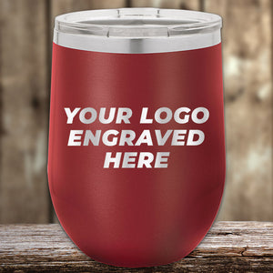 A Kodiak Coolers red tumbler with a silver lid rests elegantly on wood, featuring "YOUR LOGO ENGRAVED HERE" on its side. It's the perfect corporate promotional gift with laser-etched design and no setup fees.