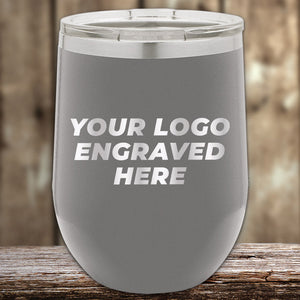 A gray custom tumbler by Kodiak Coolers, featuring an engraved logo and laser-etched design, ideal as a corporate promotional gift, is displayed on a wooden surface with a blurred wooden background.