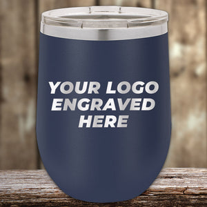 A navy blue Kodiak Coolers insulated tumbler with a clear lid sits on a wooden surface, perfect for showcasing a laser-etched logo. "Custom Tumblers with Logo Engraved" blend practicality and personalization, ideal for corporate gifts. No setup fees; limited time offer.