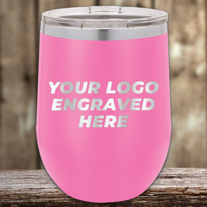 A pink Kodiak Coolers insulated tumbler with a silver lid rests on wood, showcasing "YOUR LOGO ENGRAVED HERE" in white. Ideal as a corporate gift or personalized keepsake, this custom tumbler presents a laser-etched design without setup fees and is currently available for a limited time.