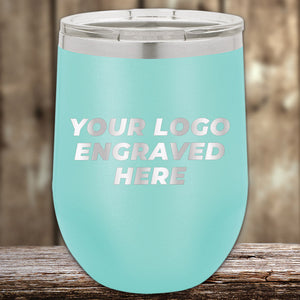 On a wooden surface sits a turquoise Kodiak Coolers insulated cup with a silver lid, perfect for corporate gifts. Engraved with "YOUR LOGO HERE," these custom tumblers are an ideal choice from the "Custom Tumblers with Logo Engraved | Laser Etched Design" collection—no setup fees, limited time offer.