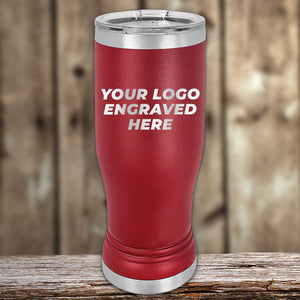 A red insulated tumbler with silver accents sits on a wooden surface, displaying the text "YOUR LOGO ENGRAVED HERE" on its front. The background consists of weathered wooden planks. Perfect for those considering Kodiak Coolers' Custom Pilsner Tumblers 14 oz with your Logo or Design Engraved | No Minimal Order | Sample Volume Pricing or bulk wholesale pricing for a uniform look.