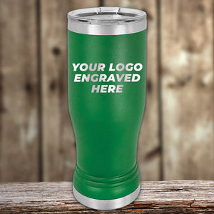 A green stainless steel Custom Pilsner Tumbler 14 oz with your Logo or Design Engraved from Kodiak Coolers with a silver lid is shown against a wooden background. The tumbler, ideal for bulk wholesale pricing, has the text "YOUR LOGO ENGRAVED HERE" in white capital letters.