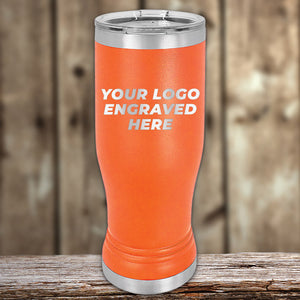 Orange stainless steel Custom Pilsner Tumblers 14 oz with your Logo or Design Engraved by Kodiak Coolers, featuring a silver lid and the text "Your Logo Engraved Here" in white lettering, placed on a wooden surface with a blurred wood panel background. Perfect for businesses seeking bulk wholesale pricing.