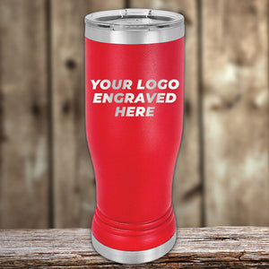 A red, stainless steel Custom Pilsner Tumbler 14 oz with your Logo or Design Engraved by Kodiak Coolers, standing on a wooden surface against a blurred wooden background. Ideal for businesses seeking bulk wholesale pricing for custom engraved products.