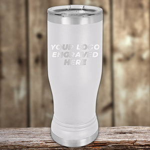 A white stainless steel tumbler with a lid, placed on a wooden surface, featuring the words "Your Logo Engraved Here." Perfect for those seeking Kodiak Coolers Custom Pilsner Tumblers 14 oz with your Logo or Design Engraved | No Minimal Order | Sample Volume Pricing or items with engraved logos at bulk wholesale pricing.