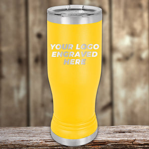 A yellow Kodiak Coolers Custom Pilsner Tumblers 14 oz with your Logo or Design Engraved featuring the words "Your Logo Engraved Here" in white text on the front. Perfect for bulk wholesale pricing and custom pilsner glasses collections, it’s set against a blurred wooden surface background.