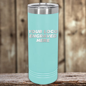 A Kodiak Coolers' teal tumbler with laser-etched "Your Logo Engraved Here" text elegantly sits on a wooden surface, against a blurred wooden backdrop. Enjoy this custom tumbler with no setup fees—available for a limited time!.