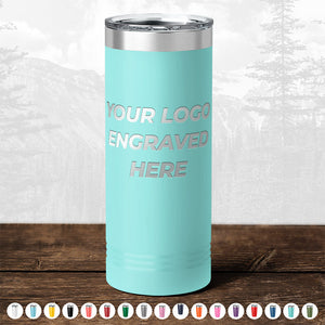 A teal tumbler from Kodiak Coolers, featuring the engraving "YOUR LOGO HERE," sits on a wooden surface, making it an ideal promotional gift. A selection of personalized mugs in various colors is arranged below it.