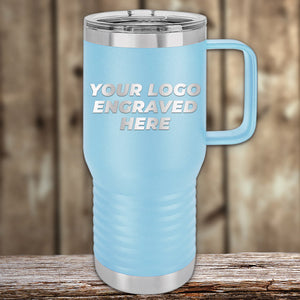 On a wooden surface stands a light blue Kodiak Coolers custom tumbler with a handle, featuring "Your Logo Engraved Here" in silver. This laser-etched design makes it an ideal corporate promotional gift.