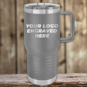 A gray Kodiak Coolers travel mug with a handle and "Your Logo Engraved Here" text rests on a wooden surface, harmonizing with the rustic background. This custom tumbler makes a perfect corporate promotional gift. Available as part of our limited-time offer for laser-etched designs, with no setup fees!.