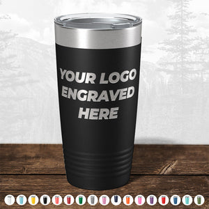 A customizable black travel tumbler, featuring the text "YOUR LOGO ENGRAVED HERE," is displayed on a wooden surface alongside various color options. This promotional gift from Kodiak Coolers, named "Custom Drinkware Engraved with your Logo or Design - Front Side Logo Included," is perfect for showcasing your brand on personalized mugs. Don't miss out on our HUGE LABOR DAY SALE - ENDS TODAY!