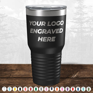 A black travel tumbler from Kodiak Coolers with the text "YOUR LOGO ENGRAVED HERE" on it, surrounded by various color options displayed at the bottom. Perfect as a promotional gift, the background features an outdoor, forested landscape. Custom Drinkware Engraved with your Logo or Design - Front Side Logo Included - HUGE LABOR DAY SALE - ENDS TODAY!