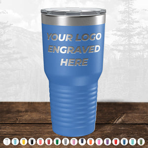 A blue insulated tumbler from Kodiak Coolers, featuring the text "Your Logo Engraved Here" on it, is displayed against a mountain landscape backdrop. This makes it an ideal promotional gift. Various color options are shown at the bottom for your personalized mugs selection. Don't miss out on the HUGE LABOR DAY SALE - ENDS TODAY!