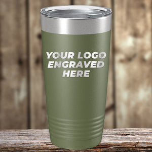 A green travel tumbler with a silver lid is placed on a wooden surface. The text "YOUR LOGO ENGRAVED HERE" is laser engraved on the front. The background is a blurred wooden texture, perfect for showcasing Kodiak Coolers Custom Tumblers 20 oz with your Logo or Design Engraved - Special Bulk Wholesale Pricing - Bundle Packs available at wholesale pricing.