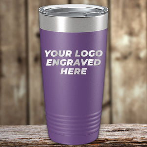 A purple travel mug with a silver lid and the text "Your Logo Engraved Here" on the front. The Kodiak Coolers Custom Tumblers 20 oz with your Logo or Design Engraved - Special Bulk Wholesale Pricing - Bundle Packs is placed on a wooden surface with a wood-paneled background, perfect for businesses looking for wholesale pricing options.