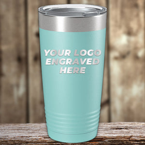 A light blue, stainless steel tumbler with a lid displayed against a wooden background. The text on the tumbler reads "Your Logo Engraved Here." These Custom Tumblers 20 oz with your Logo or Design Engraved - Special Bulk Wholesale Pricing - Bundle Packs can be laser engraved and are available at wholesale pricing from Kodiak Coolers.