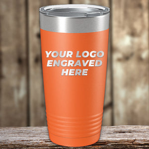 Orange insulated tumbler with a silver lid, standing on a wooden surface. The words "Your Logo Engraved Here" are printed on the tumbler in white text. These Custom Tumblers 20 oz with your Logo or Design Engraved - Special Bulk Wholesale Pricing - Bundle Packs from Kodiak Coolers feature laser engraving for precision and durability. Background shows blurred wooden panels.