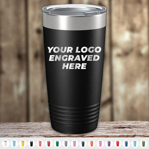 A black Kodiak Coolers Custom Tumbler 20 oz with your Logo or Design Engraved - Special Bulk Wholesale Pricing - Bundle Packs, meticulously laser engraved. There are various color options displayed below the custom tumbler. The background is a blurred wooden surface, and wholesale pricing is available.