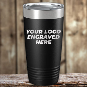 A black Kodiak Coolers Custom Tumblers 20 oz with your Logo or Design Engraved - Special Bulk Wholesale Pricing - Bundle Packs with a silver lid and the text "YOUR LOGO ENGRAVED HERE" displayed on its front. The laser engraved tumbler is placed on a wooden surface with a blurred wooden background, perfect for bulk orders of wholesale custom tumblers.