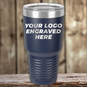 A navy blue Kodiak Coolers Custom Tumblers 30 oz with your Logo or Design Engraved | No Minimal Order | Sample Volume Pricing stands on a wooden surface, set against a blurred wooden background. These promotional items make for perfect giveaways and gifts.