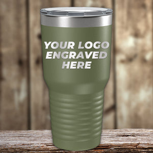 A green Custom Tumblers 30 oz with your Logo or Design Engraved by Kodiak Coolers, placed on a wooden surface with a blurred wooden background, makes for exceptional promotional items.