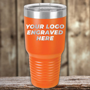 An orange Kodiak Coolers Custom Tumbler 30 oz with a silver lid and the text "Your Logo Engraved Here" displayed on the front, placed on a wooden surface. This custom tumbler makes an ideal choice for promotional items.