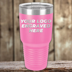 A pink, stainless steel insulated tumbler with a clear lid, displayed on a wooden surface. The text on the Kodiak Coolers Custom Tumblers 30 oz with your Logo or Design Engraved reads "YOUR LOGO ENGRAVED HERE." Ideal for promotional items.