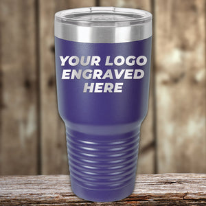 A blue insulated tumbler with a stainless steel lid sits on a wooden surface, showcasing the text "YOUR LOGO ENGRAVED HERE." Perfect for custom tumblers or promotional items. This is the Custom Tumblers 30 oz with your Logo or Design Engraved | No Minimal Order | Sample Volume Pricing by Kodiak Coolers.