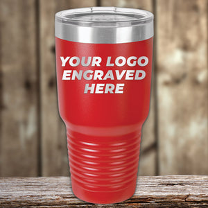 Red stainless steel Custom Tumblers 30 oz with your Logo or Design Engraved by Kodiak Coolers with the text "YOUR LOGO ENGRAVED HERE" on its side. The tumbler is placed on a wooden surface with a blurred background, making it an ideal promotional item.