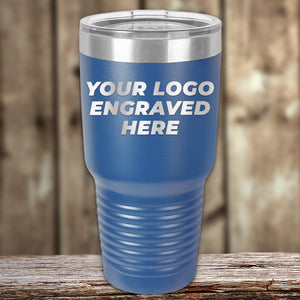 A blue insulated Kodiak Coolers Custom Tumblers 30 oz with your Logo or Design Engraved | No Minimal Order | Sample Volume Pricing with a transparent lid sits on a wooden surface, displaying the engraved logo "YOUR LOGO ENGRAVED HERE." Perfect for promotional items and custom tumblers.