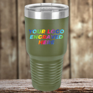 A green Kodiak Coolers insulated travel tumbler with a clear lid is shown on a wooden surface, featuring the text "YOUR LOGO ENGRAVED HERE" in full rainbow-colored print on the front. Perfect for custom tumblers and ideal as a corporate promotional gift, these Custom Tumblers - UV Printed with your Logo or Design in Full Color are available for a limited time offer with a $250 minimum order.