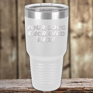 A white insulated tumbler with a clear lid is placed on a wooden surface. The Kodiak Coolers Custom Tumblers 30 oz with your Logo or Design Engraved  | No Minimal Order | Sample Volume Pricing has the text "Your Logo Engraved Here" displayed on it, making it an ideal promotional item.
