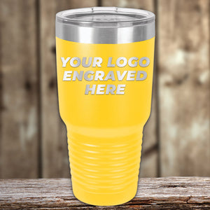 A yellow Custom Tumblers 30 oz with your Logo or Design Engraved | No Minimal Order | Sample Volume Pricing from Kodiak Coolers with a silver lid and "Your Logo Engraved Here" text on the front. Perfect as promotional items, it is placed on a rustic wooden surface with a blurred wooden background.