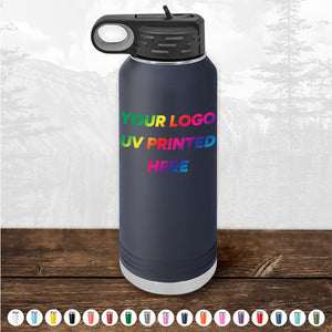 A Custom Tumbler from Kodiak Coolers featuring a handle cap and UV-printed text "YOUR LOGO UV PRINTED HERE" in a rainbow gradient, set against a backdrop of pine trees in a forest. This black water bottle makes an ideal corporate promotional gift and is available for a limited time with a $250 minimal order.