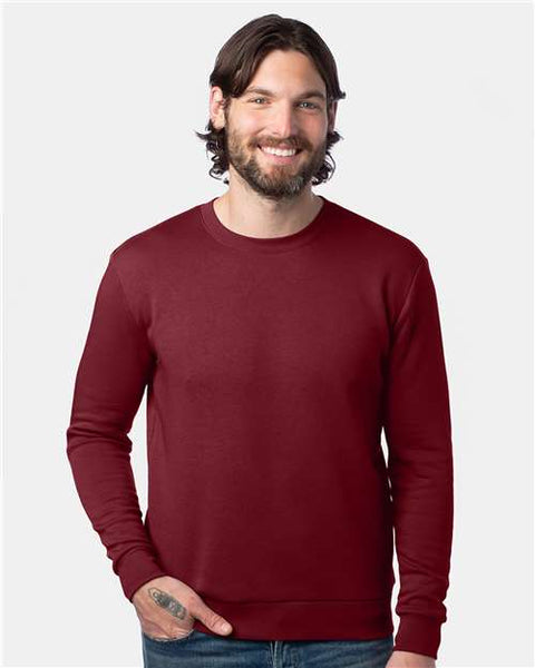 A man with long hair and a beard, wearing an Alternative Eco-Cozy Fleece Crewneck Sweatshirt made from recycled materials and jeans, poses against a plain white background with a smile.