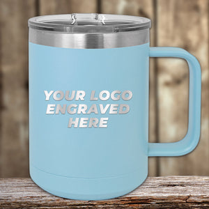 A light blue insulated mug from Kodiak Coolers with a handle and a clear lid, placed on a wooden surface. The Engraved Custom Logo Drinkware - SPECIAL 72 HOUR SALE PRICING - Single Side Engraving Included in Price O features the text "YOUR LOGO ENGRAVED HERE" prominently on the side, making it an ideal promotional gift.