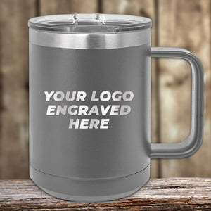 The engraved Custom Logo Drinkware by Kodiak Coolers is a stylish gray insulated mug with a handle. It features a customizable area labeled "Your Logo Engraved Here," and is displayed on a wooden surface with a blurred wooden background. This personalized mug, now available at special 72-hour sale pricing with single-side engraving included, makes an ideal promotional gift for any occasion.