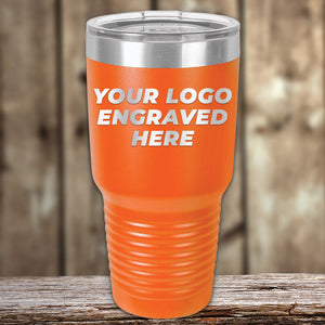 A Kodiak Coolers Engraved Custom Logo Drinkware tumbler in orange, featuring a silver lid and the text "YOUR LOGO ENGRAVED HERE" on the front, is displayed. Ideal as a promotional gift, it is placed on a wooden surface with a blurred wooden background. This product benefits from SPECIAL 72 HOUR SALE PRICING with single side engraving included in the price.