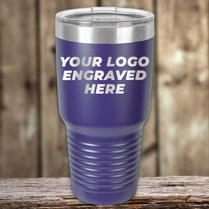 A purple Engraved Custom Logo Drinkware tumbler by Kodiak Coolers, featuring a clear lid, rests on a wooden surface. The text "YOUR LOGO ENGRAVED HERE" is printed on the tumbler. The background showcases a blurred wooden wall, making it an ideal promotional gift for personalized mug enthusiasts. Take advantage of the SPECIAL 72 HOUR SALE PRICING with single side engraving included in the price!